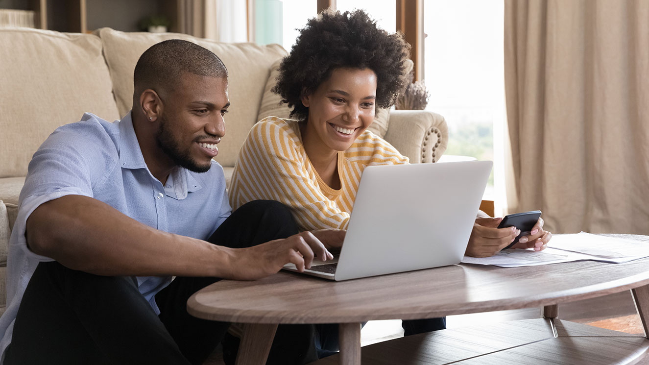 Two people sitting together viewing a laptop monitor.