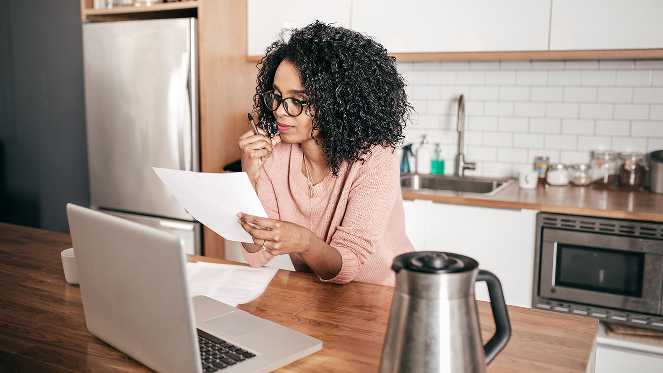 Woman standing in her kitchen and using her laptop to pay a bill.