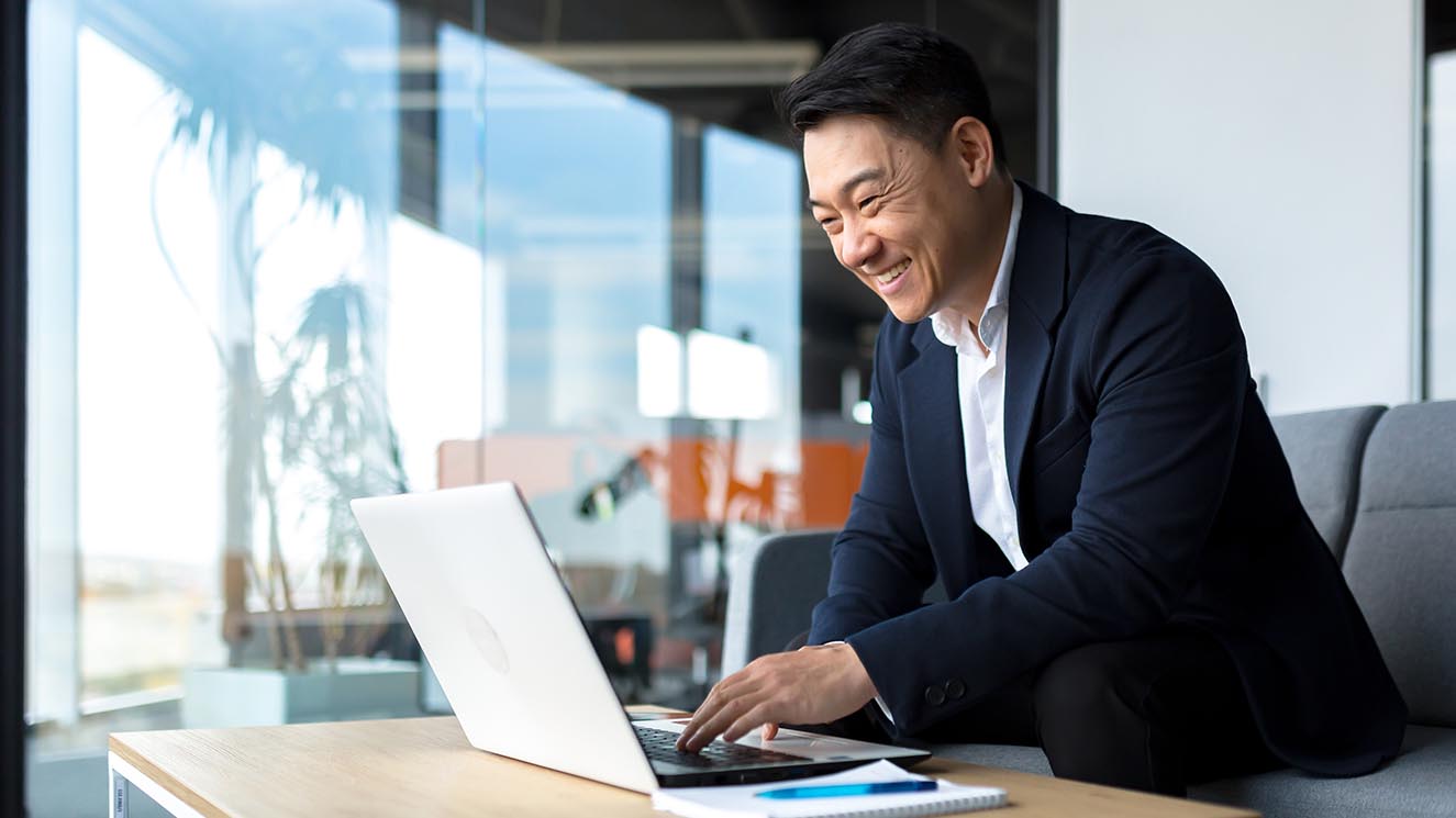 Asian man in a suit doing commercial receivables work on a laptop.