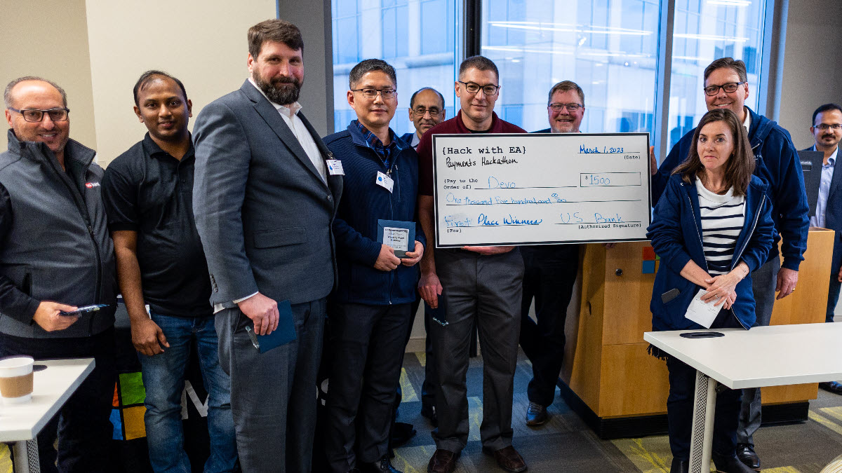 Several people standing in a line and smiling at a camera, three of which are holding a giant check.