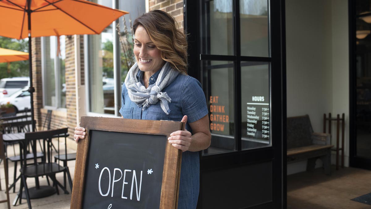 Photo of woman business owner placing open sign in front of her cafe