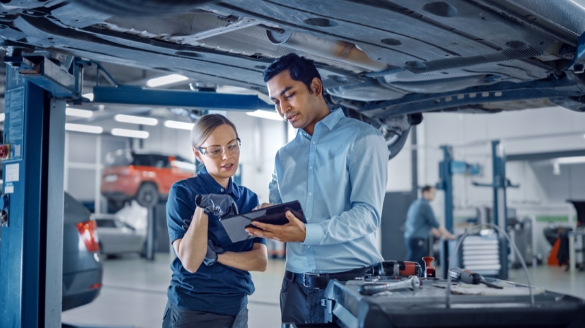 Two people smiling while looking at a tablet in a workshop