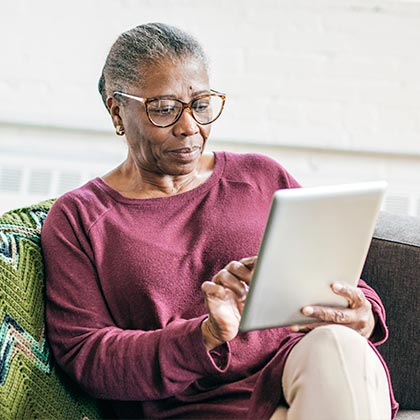 Elderly woman sitting on a chair and using a tablet device.