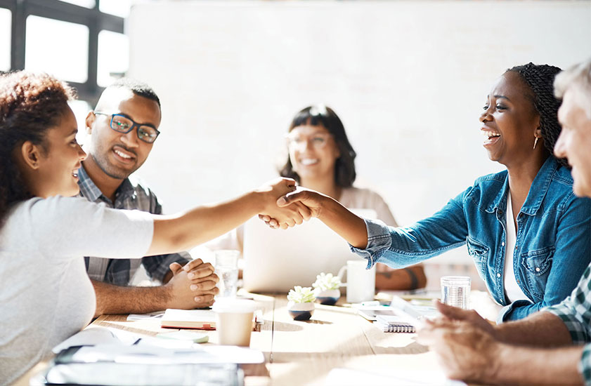 Group of five diverse people around table, two of them shaking hands.