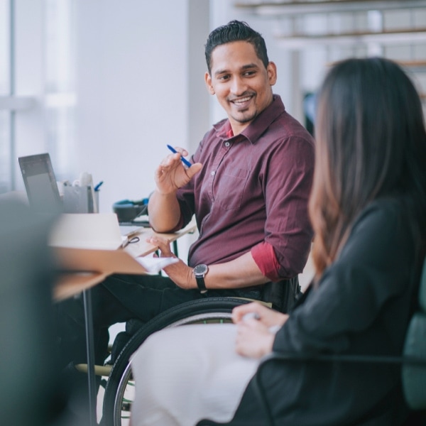 Person in wheelchair at a desk with their body turned talking to another person