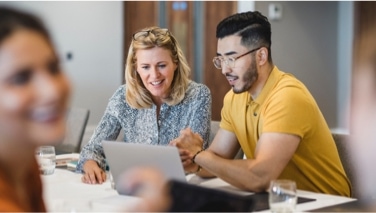 Two people sitting at a table talking to each other while one points at a laptop