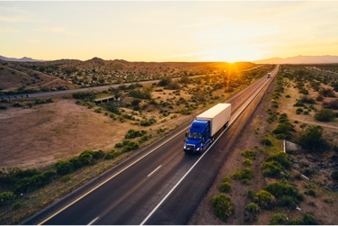 Freight truck driving down highway with a sunset in the background 