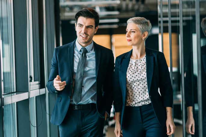 Male and female coworkers dressed in suits and walking together down a hallway at an office.