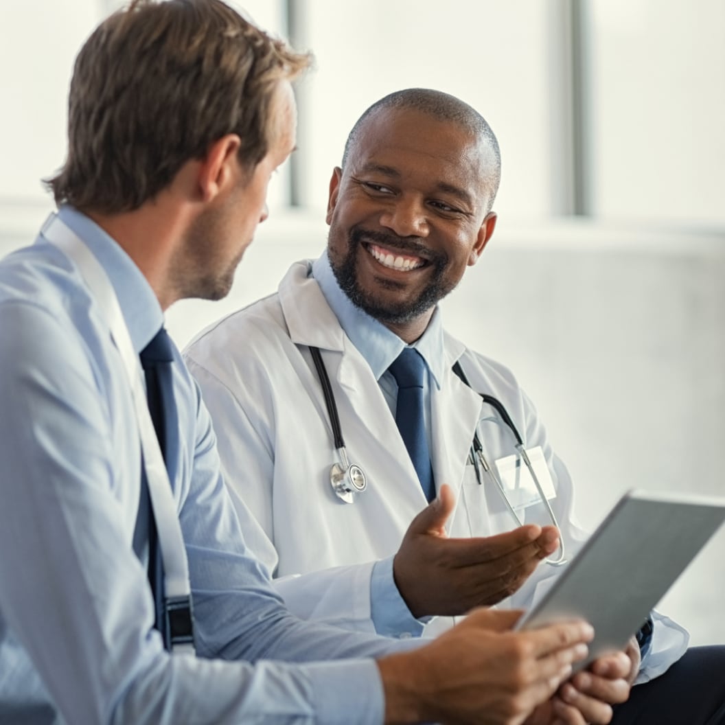 Image of a doctor and a healthcare administrator sitting next to each other. The doctor has a stethoscope and the administrator is holding a tablet device.