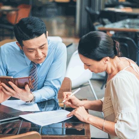 Man and woman, professionally dressed, sitting at a table together and looking at documents.