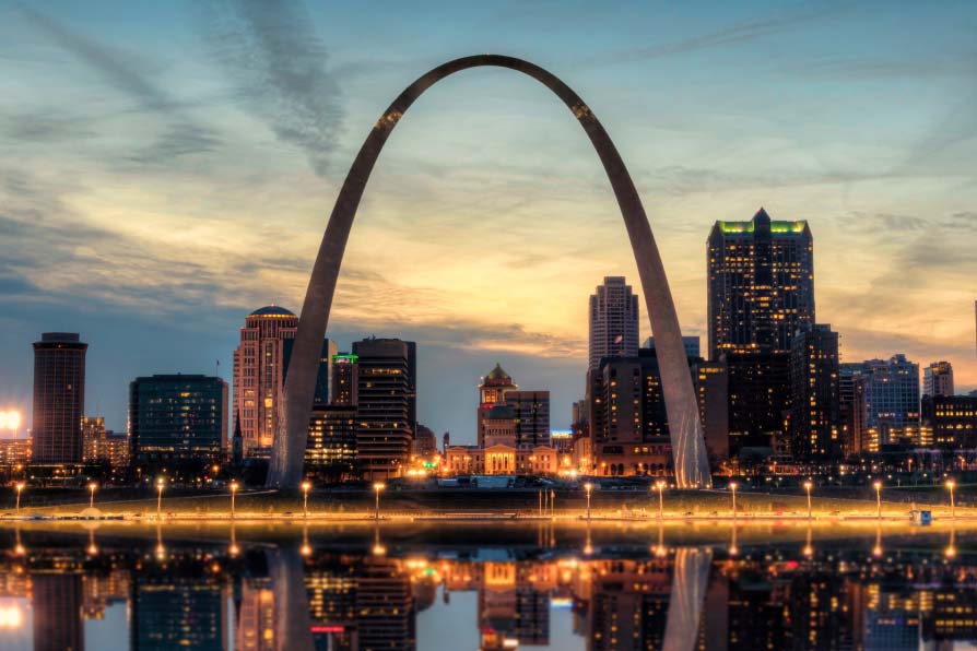 The St. Louis Arch at night with city lights in the background.