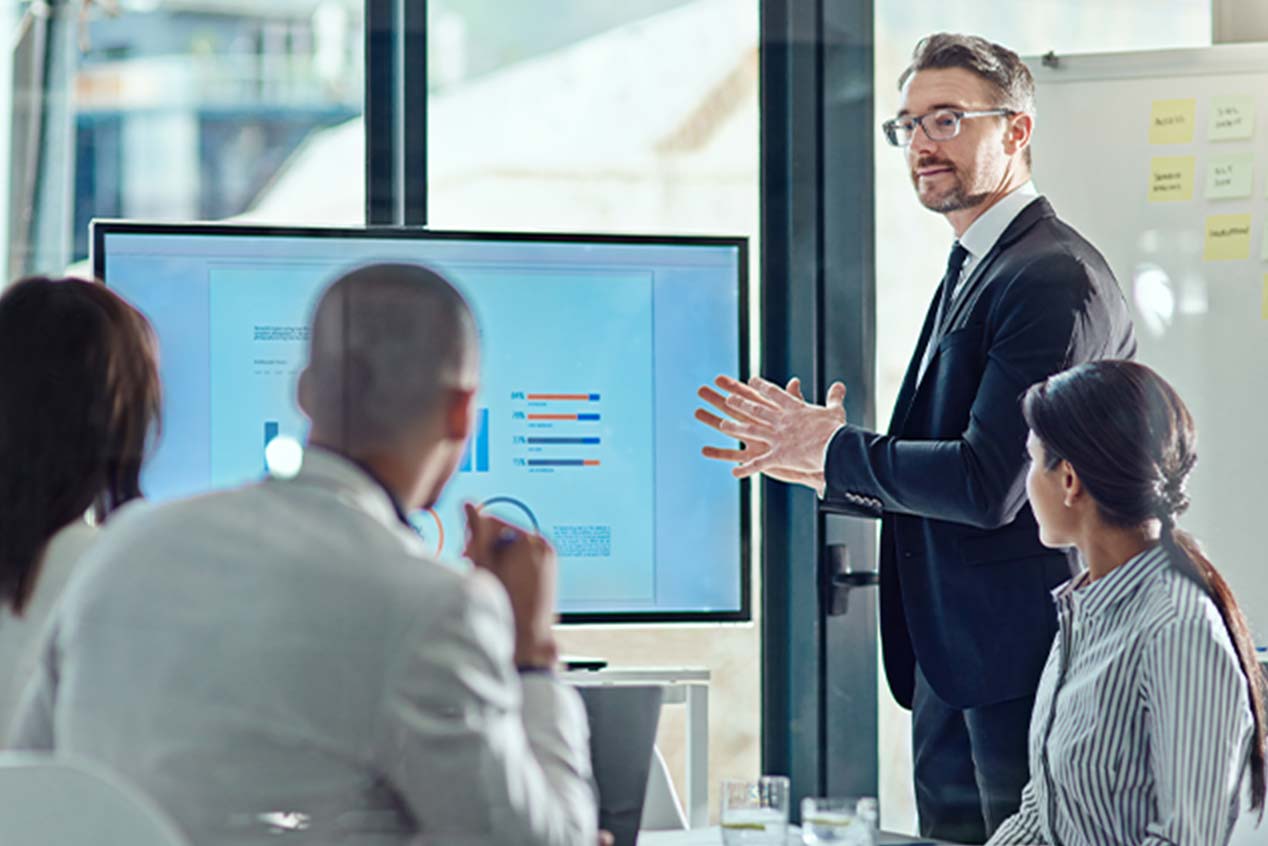 Man in suit standing in front of colleagues and giving a presentation at work.