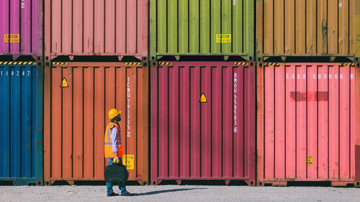 Photo of worker walking in front of shipping containers