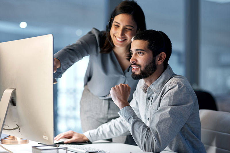 Two young professionals, one male and one female, who are looking at a computer monitor together as they discuss the order to cash cycle