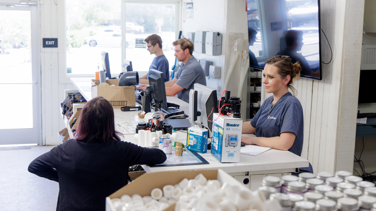 Three employees and a customer at the counter of an irrigation equipment store.