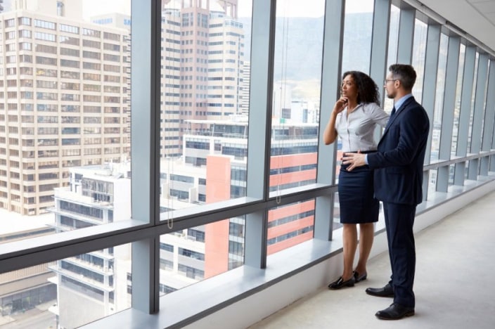 Man and woman standing inside an office tower looking out the window.