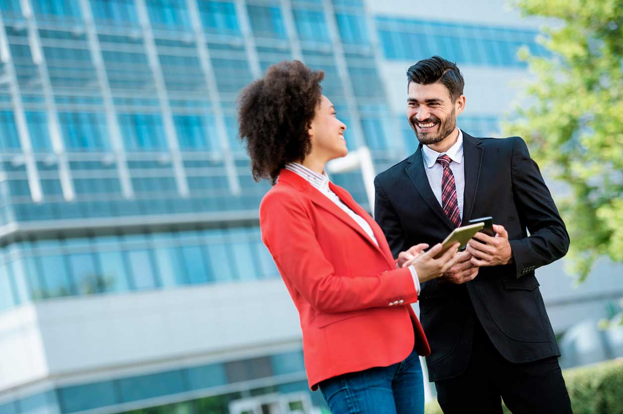 Professionally dressed man and woman standing together outside a large glass office building.