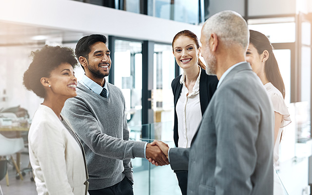 Group of 3 women and 2 men, all dressed professionally, and talking outside of an office.