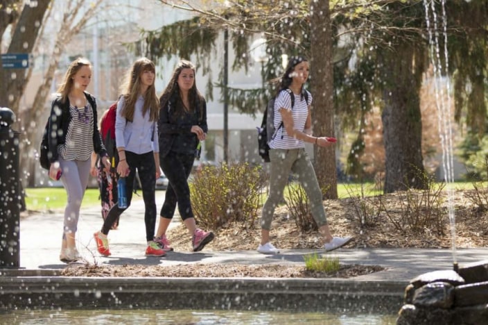 Four female college students walking together across a college campus.