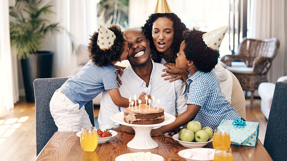 A mother and two children celebrate Dad’s birthday with a cake and party hats.