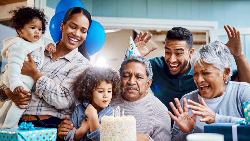 A mother and two children celebrate Dad’s birthday with a cake and party hats.